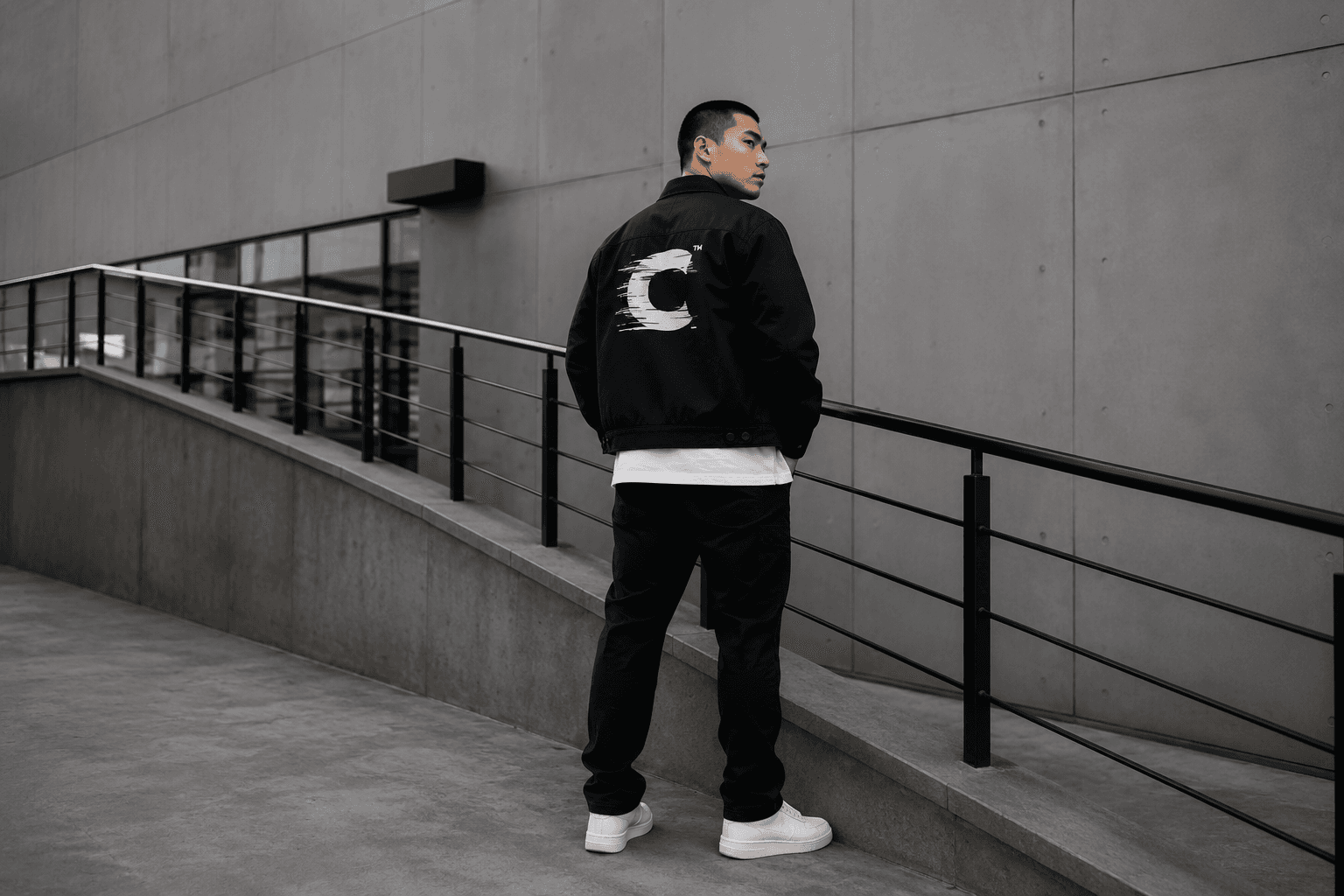 Model wearing a custom-printed black work jacket on concrete steps